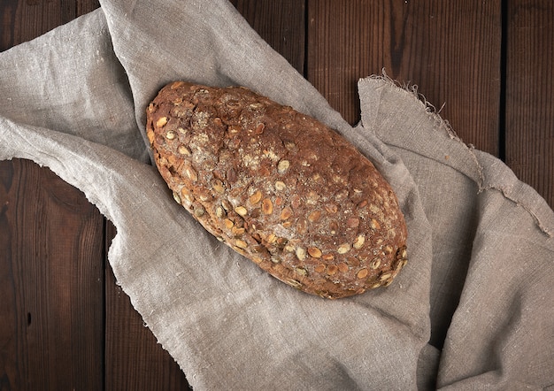Pão oval cozido, feito de farinha de centeio com sementes de abóbora em um guardanapo de linho cinza, vista superior