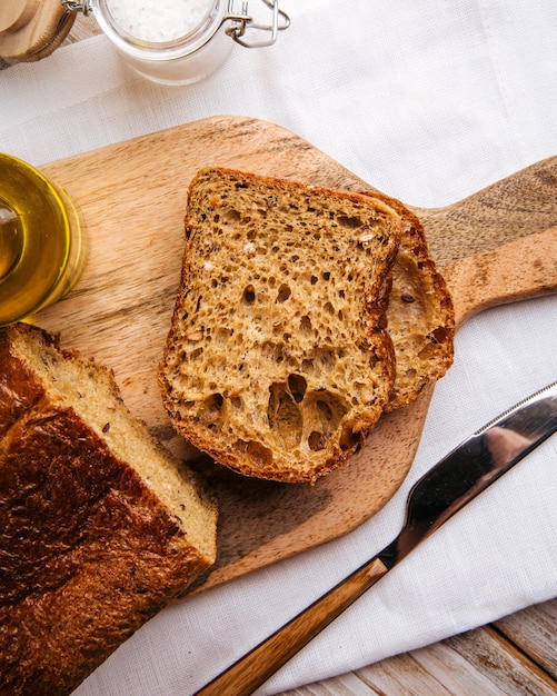 Pão preto fatiado em tábua de madeira com azeite de oliva