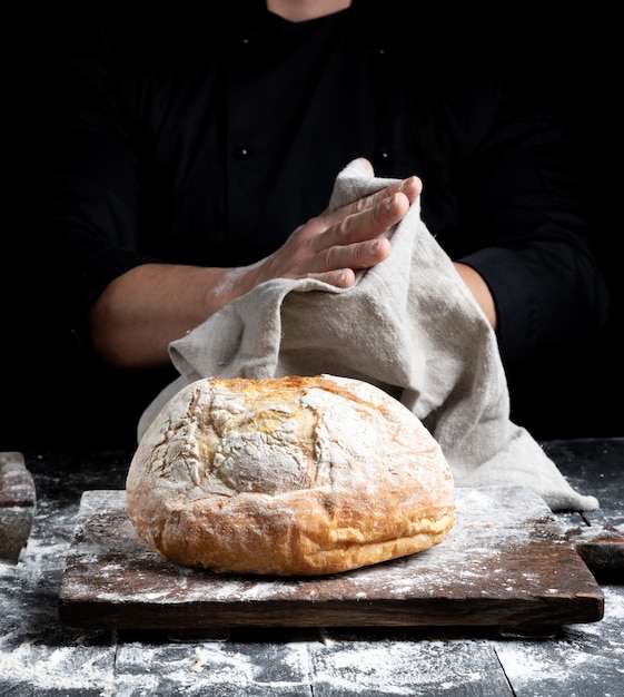 Pão redondo assado em uma placa atrás do cozinheiro em roupas pretas