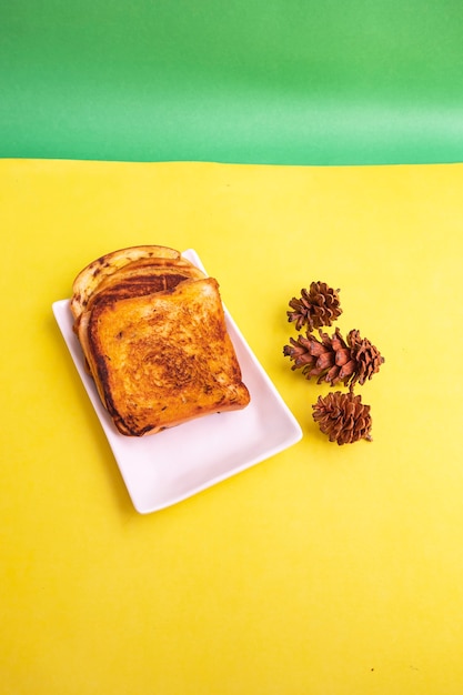 Pão torrado em um prato branco com flores de abeto em um fundo de papel amarelo e verde. brinde no café da manhã. foto vertical