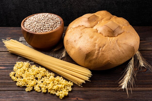 Pão, trigo e macarrão em fundo escuro de madeira