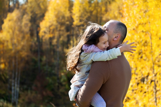 Papá abrazando a joven hija en el parque otoño