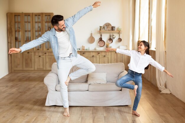 Papá alegre e hija bailando haciendo movimientos divertidos en casa