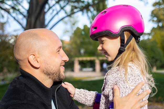 Papá alegre y pequeña hija en un casco abrazándose en el parque