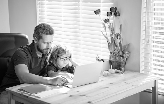 Papá ayudando a su hijo de la escuela con anteojos a estudiar con la computadora en casa