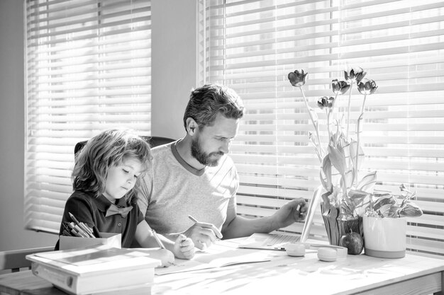 Papá barbudo escribiendo la tarea escolar con su hijo en el día de la familia en el aula