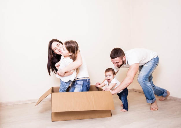 El papá y el bebé empujan una caja de cartón con mamá e hija en la habitación.