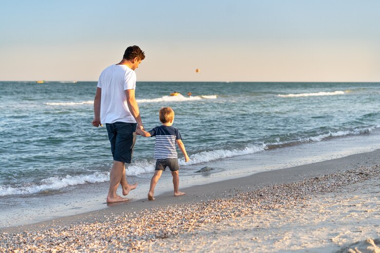 Papá caucásico joven con pequeño hijo caminar cálido día de verano a lo largo de la costa del mar. Concepto de vacaciones familiares de verano. Amistad padre e hijo. Infancia feliz en la playa con los padres. espacio libre para texto