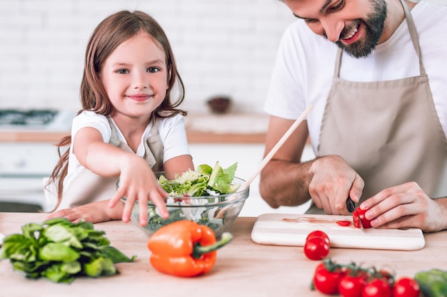 Papá cortando tomates con una chica mirando a la cámara en la cocina