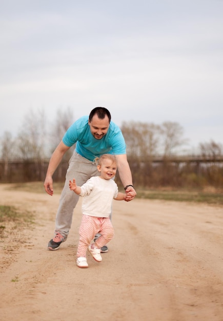 Papá cuida a su hija observándola de cerca. Al niño sonriente le encanta aprender a caminar y correr, las relaciones familiares. Papá e hija están jugando. Los primeros pasos del niño.