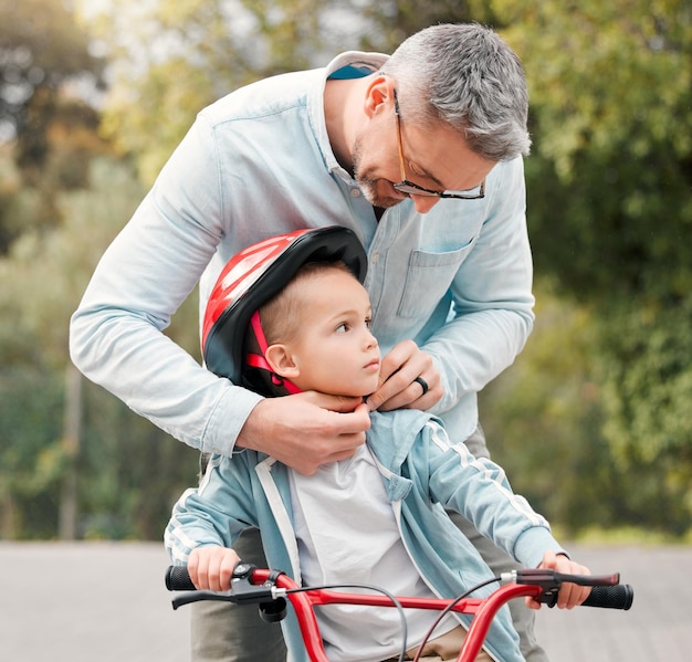 Papá dice que siempre debo estar a salvo. Fotografía de un niño pequeño sentado en su bicicleta mientras su padre se ata el casco.