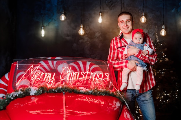 Papá e hija en el estudio un año nuevo. Familia cerca de coche rojo retro es feliz en invierno.