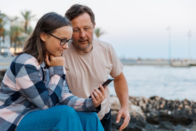 Papá e hija miran el teléfono en un paseo por la ciudad nocturna junto al mar