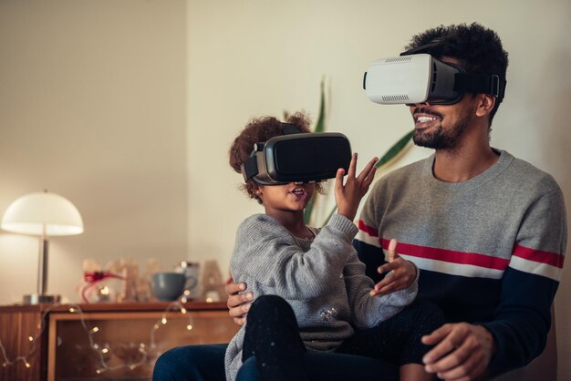 Papá e hija usando auriculares VR mientras están sentados al lado del árbol de Navidad