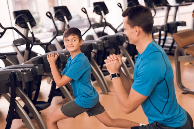 Papá e hijo atletas hacen zancadas en el gimnasio.