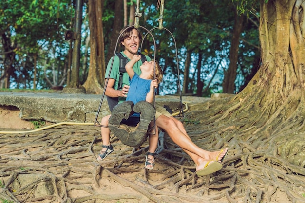 Papá e hijo columpiándose en un viejo columpio con el telón de fondo de las raíces del árbol.