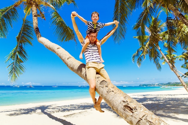 Papá e hijo se divierten en un cocotero en una playa tropical de arena. El concepto de viajes y vacaciones familiares.