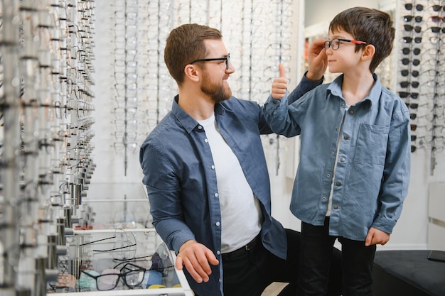 Papá e hijo eligen nuevas gafas con estilo en una tienda óptica Concepto de cuidado de la visión