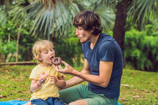 Papá e hijo están comiendo una rosquilla en el parque. Nutrición nociva en la familia.