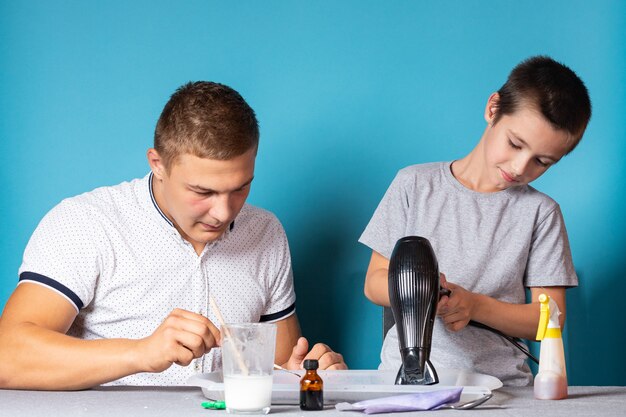 Papá e hijo están realizando experimentos químicos, observando el cambio de color de un camaleón como resultado de la reacción química del yodo y el almidón en casa. Chico se seca con un resultado de secador de pelo