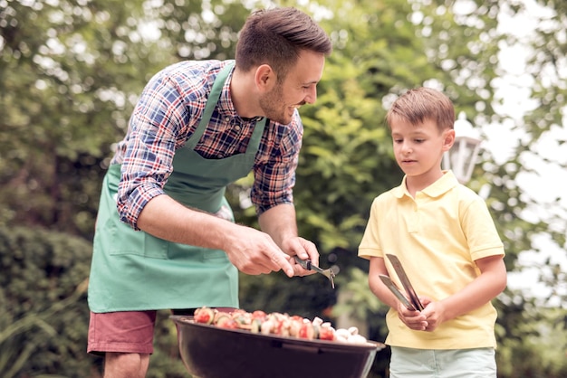 Papá e hijo haciendo una barbacoa en su jardín en verano