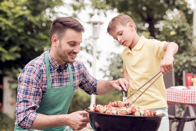 Papá e hijo haciendo una barbacoa en su jardín en verano