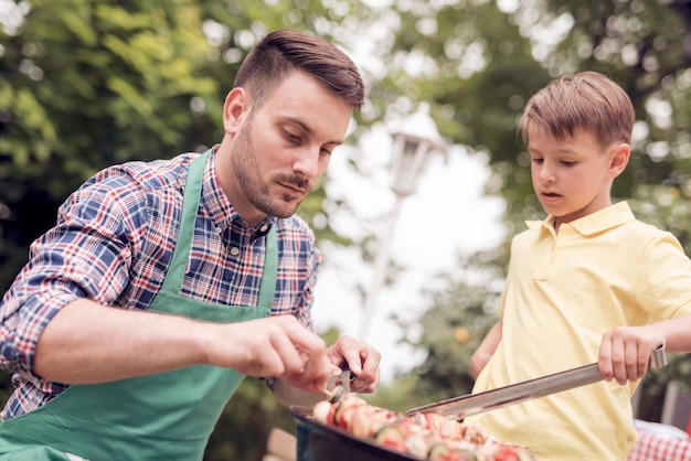 Papá e hijo haciendo una barbacoa en su jardín en verano