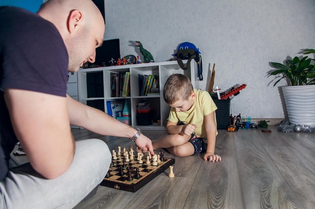 Papá e hijo juegan al ajedrez en el suelo de la habitación de los niños entre los juguetes.