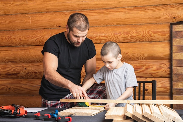 Foto papá e hijo miden con cinta bloques de madera, planificando cómo construir una casa para pájaros