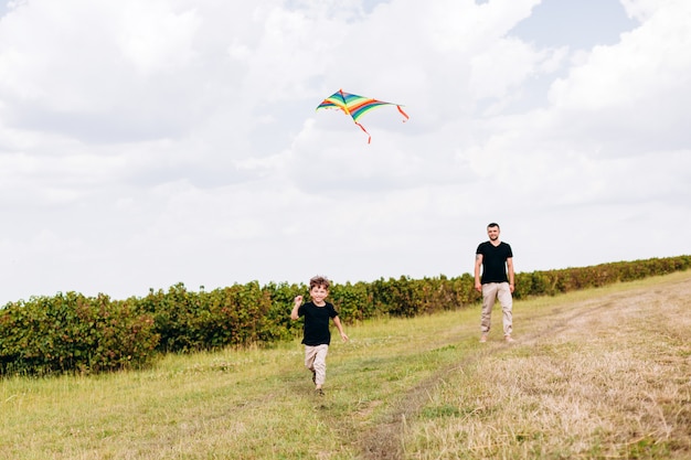 Papá e hijo pasando un rato divertido, lanzan una cometa sobre la naturaleza