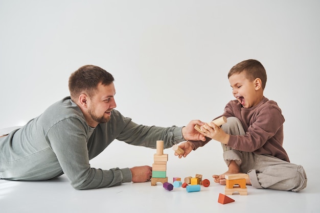 Foto papá e hijo sonriendo divirtiéndose y jugando con ladrillos de colores sobre fondo blanco paternidad padre cariñoso con su hijo