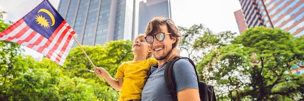 Papá e hijo turistas en malasia con la bandera de malasia cerca de los rascacielos que viajan con niños