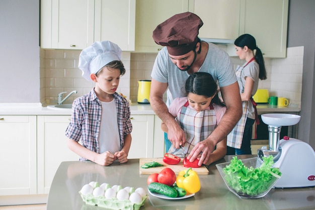 Papá le enseña a una chica caliente a cortar tomates. El la ayuda. El muchacho lo mira. El esta concentrado. La mujer se para detrás de ellos y cocina.