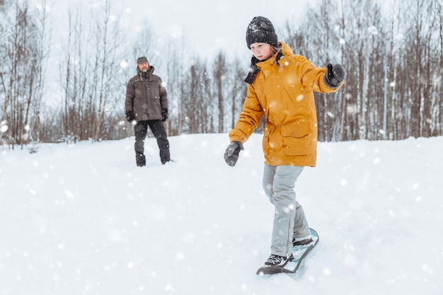 Papá le enseña a su hija a andar en patines de nieve en un parque de invierno. Paseo familiar al aire libre.