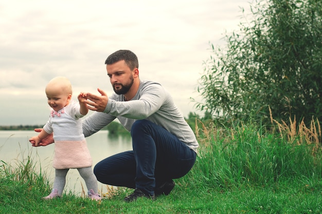 Foto papá le enseña a su hija a caminar, parque, naturaleza. camina sobre la hierba. padre e hija. primeros pasos.