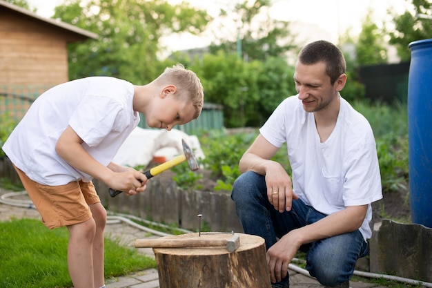 Papá le enseña a su hijo a clavar clavos en un árbol