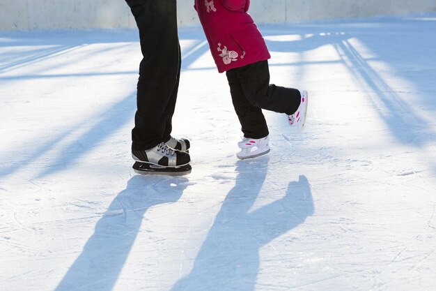 Papá le enseña a su pequeña hija a patinar sobre hielo en una pista de patinaje en el patio de los edificios de varios pisos de la ciudad. Día soleado de invierno helado, deportes de invierno activos y estilo de vida