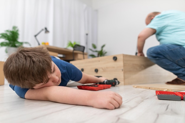 Papá está retorciendo muebles en la sala de estar y su hijo se ha quedado dormido en el suelo.