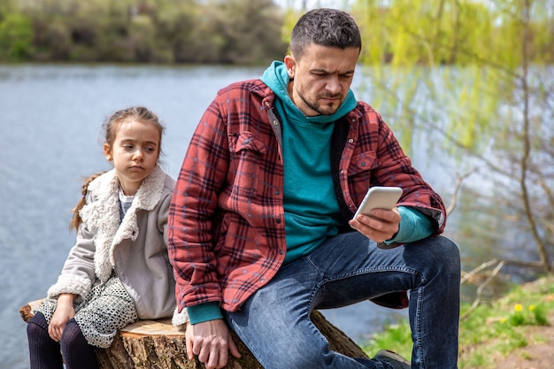 Papá está revisando su teléfono, sin prestar atención a su hija, para dar un paseo por el bosque.