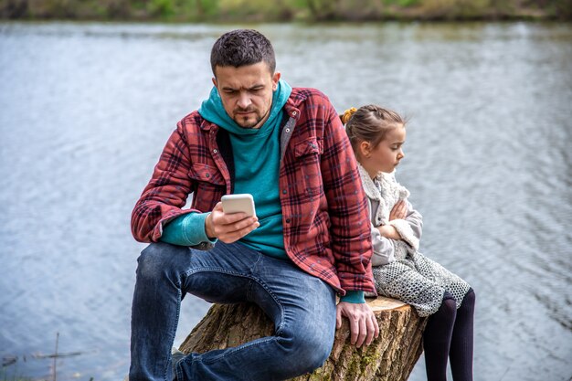 Papá está revisando su teléfono, sin prestar atención a su hija, para dar un paseo por el bosque.