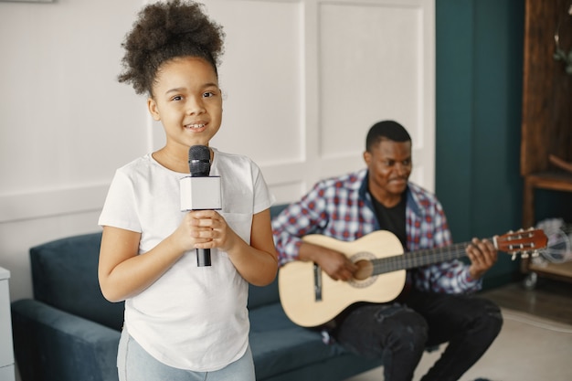 Papá está sentado con una guitarra e hija con un micrófono.