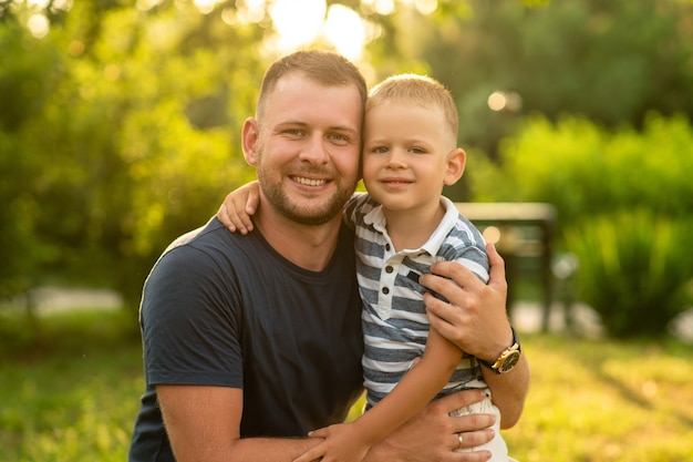 Foto papá feliz abraza felizmente a su hijo en el jardín. dia del padre. concepto de felicidad familiar, paternidad, juego al aire libre juntos.