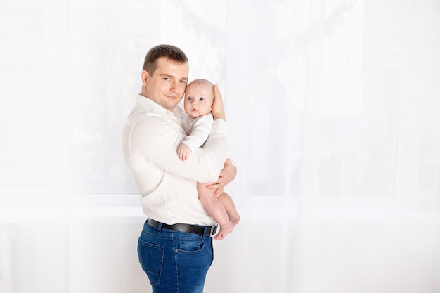 Papá feliz con bebé recién nacido en casa junto a la ventana, concepto de familia amorosa feliz, día del padre