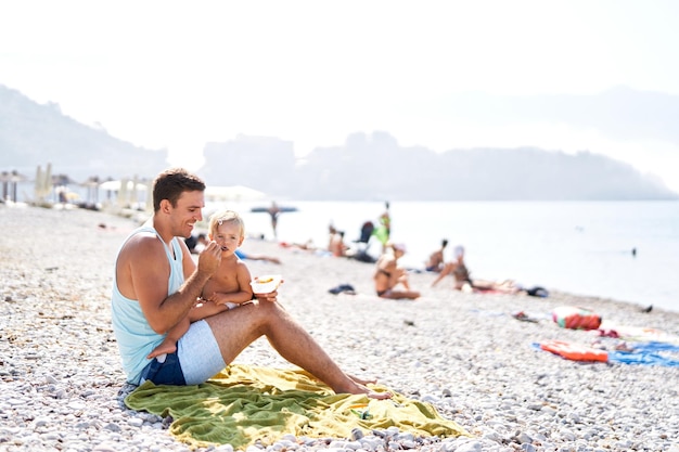 Papa füttert seine kleine Tochter am Strand mit einem Löffel