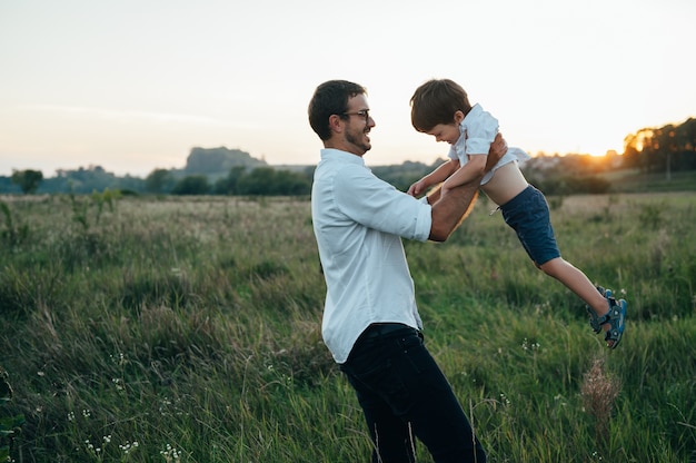 Papá guapo con su pequeño hijo lindo se divierten y juegan en el césped verde.