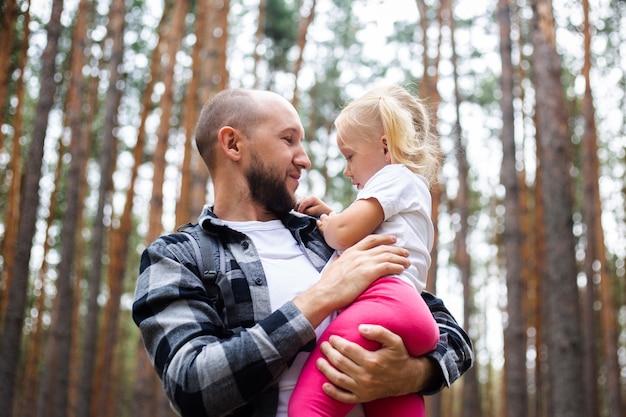 Papa hält das Baby beim Wandern im Wald in den Armen. Familienwanderung in die Berge oder in den Wald.