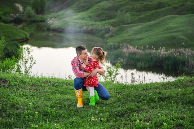 Papá con hija pequeña en botas de goma de colores brillantes en un paseo por el lago el día del padre