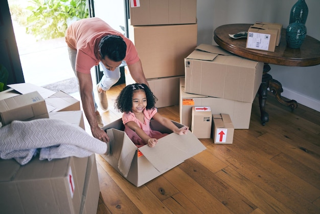 Papá, hijo y caja en un nuevo hogar para juegos, diversión y libertad en el piso de una propiedad inmobiliaria desde arriba Padre feliz, familia emocionada y niña, juegan en cajas de cartón para la carrera mientras se mudan a casa