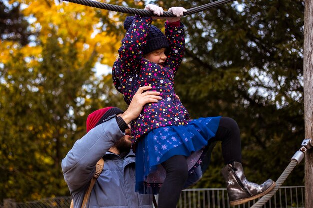 Papa hilft Tochter, im Herbstpark auf Drahtseil zu gehen