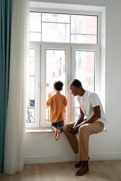 Foto papá joven mirando por la ventana con su hijo